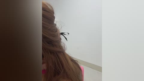 A video of a woman's back and head, showing long brown hair styled in a messy top knot with a black ribbon. She wears a pink top. The background is plain white.
