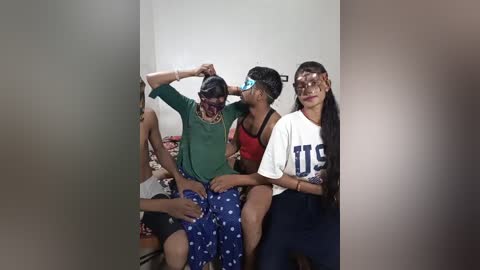 Video of three women, one in a wheelchair, wearing face masks and colorful, patterned clothing, sitting in a dimly lit hallway.