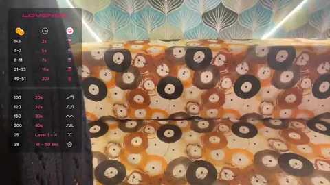Video of a wall covered in a repeating pattern of black and white record player heads on a beige background. The wallpaper also features a teal and white leaf design. A digital clock and temperature display is visible in the upper left corner.