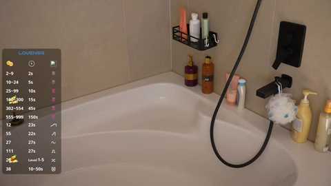 Video of a modern bathroom with beige tiled walls, a white bathtub, a showerhead, a black soap holder with bottles, and a fluffy white shower puff.