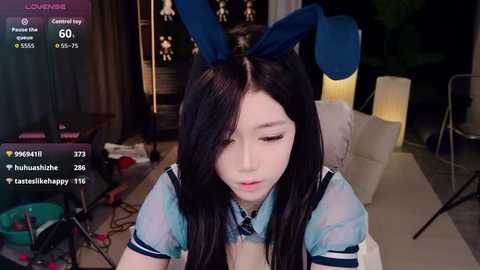 Video of an Asian woman in bunny ears and a sailor outfit, sitting in a dimly lit room with a laptop and a chair, appearing to be streaming.