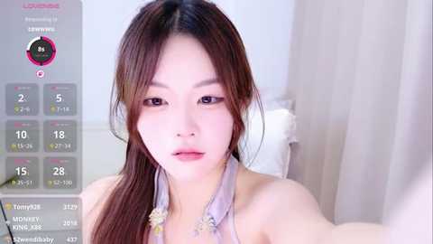 Video of a young Asian woman with long, straight brown hair, wearing a light purple halter top, taken indoors with soft lighting, showing her fair skin and subtle makeup.