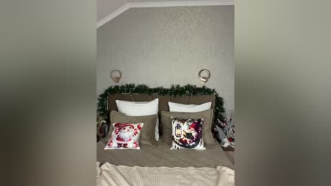 Video of a cozy, minimalist bedroom with beige walls, a beige bedspread, two pillows with Christmas-themed prints, a wreath on the wall, and a beige blanket on the bed.