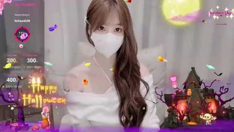 A video of a young Asian woman with long brown hair and a white mask, wearing a white off-shoulder dress, surrounded by Halloween decorations and digital overlays.