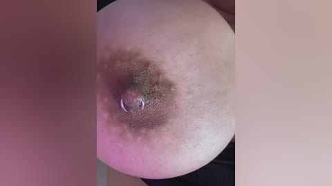 A video of a large, light-skinned woman's breast with a prominent, dark areola and nipple, positioned centrally. The skin texture is detailed, and the background is blurred.