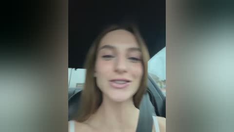 Video of a young Caucasian woman with light skin, straight brown hair, and a neutral expression, seated in a car.