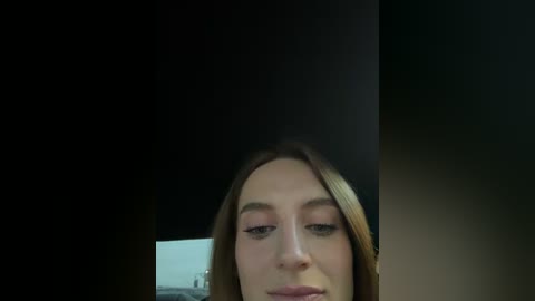 Video of a close-up of a young woman with fair skin and long brown hair, slightly cropped, wearing light makeup, against a dark background.