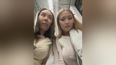 Video of two young women, one with long dark hair, the other with blonde hair, seated in a subway car, looking relaxed.