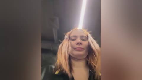 A video of a woman with light skin and long, blonde hair styled into two large, voluminous pigtails. She has a neutral expression, wearing a black jacket. The background is dimly lit, suggesting an indoor setting.