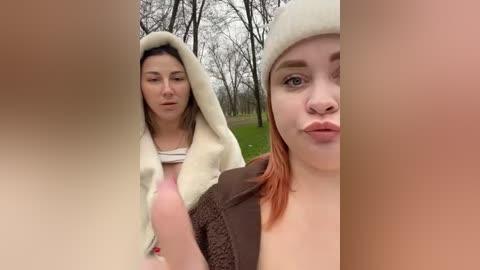 A video featuring two women in a park, one wearing a fluffy white coat and hood, the other with orange hair, puckering her lips.