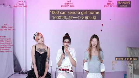 Video of three young women, one with red hair, one with black hair, and one with blonde hair, seated at a table. Background features posters with Chinese text and a digital sign reading \"1000 can send a girl home.\