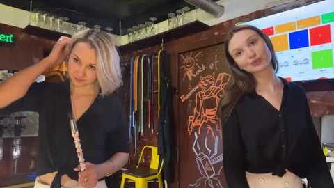 Video of two women, one blonde and one brunette, in a lively, colorful bar with chalkboard art, glassware, and a vibrant background.