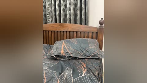A video of a neatly made bed with a dark green comforter featuring large, stylized orange leaves. The wooden headboard has vertical slats. Behind, heavy, patterned curtains in shades of gray and white.