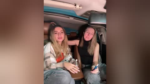 Video of two teenage girls with long hair, one in a plaid shirt and jeans, the other in a black top, sitting in a car, looking relaxed and happy.