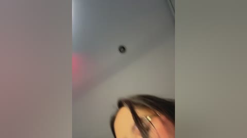 Video of a woman's face partially obscured by a large, light-colored laptop screen. The laptop's surface is smooth and reflective, casting a shadow on her face. The background is neutral and slightly blurred.