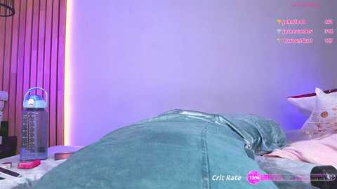 Video of a person lying on a bed, wearing green jeans, in a room with pink walls, a bottle of water, and a pillow with a floral design.