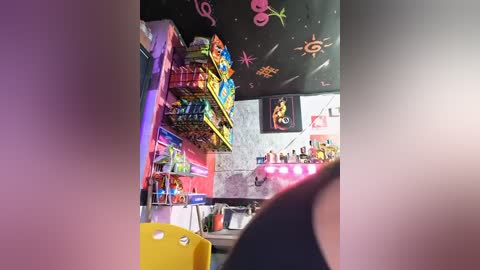 A video of a colorful, cluttered room with a black ceiling adorned with colorful stickers, shelves filled with toys, and a pink bed visible in the foreground.