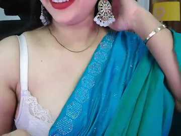 Video of a fair-skinned woman with a light complexion wearing a turquoise saree with a white lace border and a white lace bra, adorned with large, intricate silver earrings.