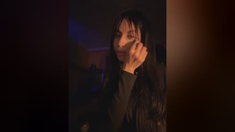 A video shows a woman with long, dark hair, wearing a black jacket, holding her face, looking distressed in a dimly lit room with warm, ambient lighting.