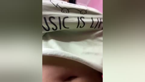 A close-up video of a person's chest, partially covered by a white t-shirt with the words \"USIC IS LIFE\" in bold black letters. The shirt appears to be worn and slightly wrinkled. The background is blurred, likely indoor lighting.