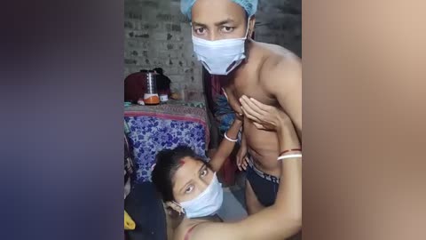 Video of a topless male with a mask, standing over a clothed woman with a mask, in a dimly lit room with a blue-patterned bedspread.