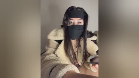 Video of a young Asian woman with long black hair, wearing a black face mask, white fluffy robe, and a black headband. She looks into a mirror, revealing a bare chest.