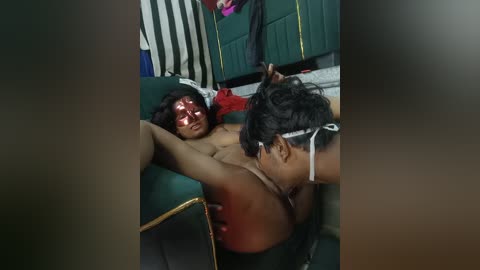 A video shows two people, a dark-skinned woman with long hair and a man with a shaved head, in a sexual act on a green couch, surrounded by a dimly lit, cluttered room.