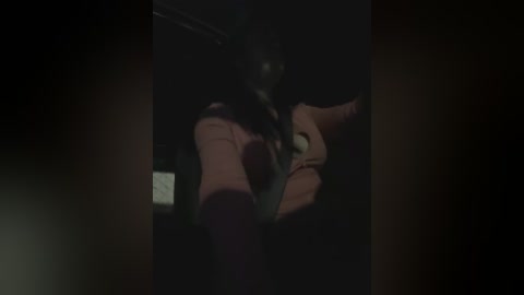 A dimly lit video captures two people in a dark, possibly indoor setting. The woman, with long dark hair, leans over the man, who is partially visible. The woman's facial expression is difficult to discern due to the low light.