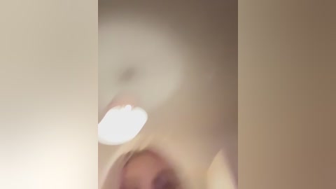 Blurry video of a person with light skin and short hair, possibly a woman, in a dimly lit room with beige walls and a ceiling light.