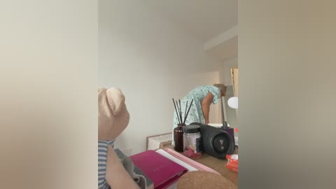 A video of a woman with short blonde hair, wearing a blue and white striped shirt, adjusting a camera on a desk in a dimly lit room.