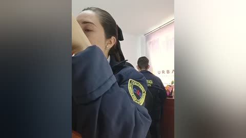 Video of two women in navy blue uniforms with yellow badges, sitting closely in a dimly lit office. One woman has her face obscured, while the other is seen from behind.