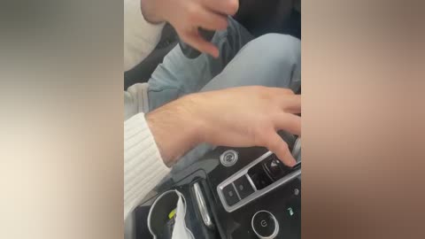 Video of a person's hands on a car dashboard, with a light gray sweater, blue jeans, and a black belt visible.