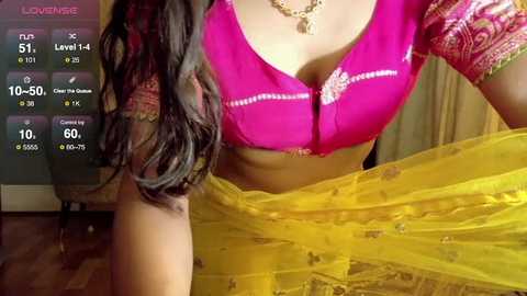 Video of a South Indian woman in a bright pink blouse with intricate embroidery, holding a yellow saree, indoors.