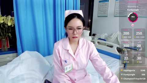 A video of an Asian woman in a nurse's uniform, with a pink hat, standing in a hospital room. The room features blue curtains and a bed with white sheets.