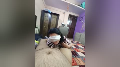Video of an Asian woman in a striped shirt performing oral sex on a man with a prominent erection. The room is modest, featuring purple walls, a bed with patterned sheets, and wooden doors.