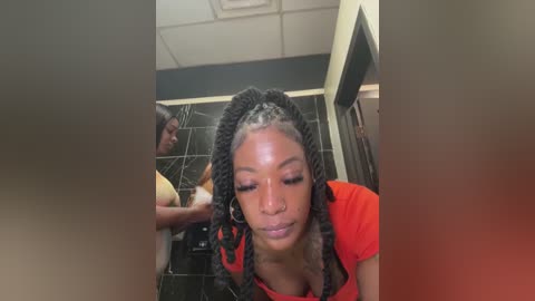 Video of a Black woman with braided hair in a bathroom, wearing a red shirt, washing her face with a white cloth.