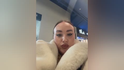 Media: A video of a young woman with light skin and brown hair, wearing a beige fur coat, captured from a low angle through a window, showing her partially obscured face.