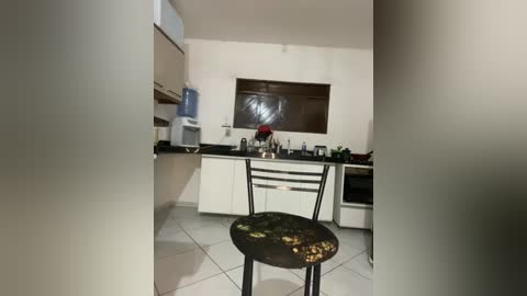 Video of a modern kitchen with white cabinets, black countertop, stainless steel appliances, and a small black wooden stool with intricate designs.