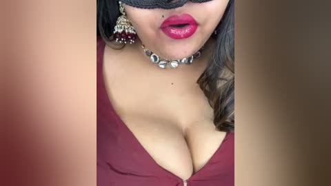 Video of a woman with light brown skin, wearing a deep red halter top, showcasing cleavage, and a black lace mask. She has full, glossy red lips and large silver hoop earrings.