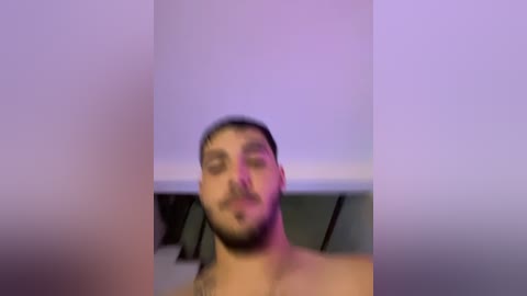 A blurry video of a young man with short dark hair and a beard, wearing a backward cap, in a dimly lit room.