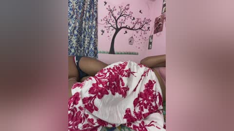 Video of a person lying on a bed with a red and white floral-patterned blanket, in a room with pink walls featuring a tree mural and butterfly decals.