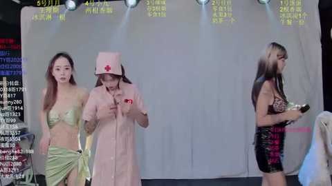 Video of a live-streamed TV show featuring a nurse in a pink uniform, two models in revealing outfits, and a blurred audience.