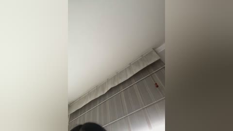 Video of a dimly lit, unfinished room with a sloped, white-painted ceiling and exposed metal beams. The floor is bare concrete, and a small red object, possibly a tool, is on the ground.