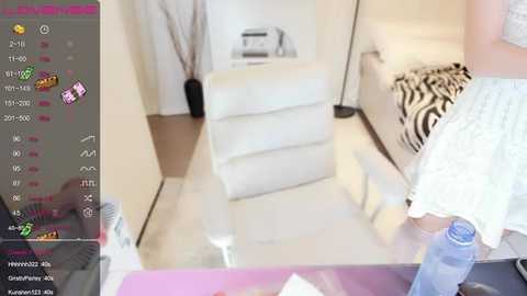 Video of a modern, minimalist living room with a white couch, zebra-patterned throw, and a woman in a white dress standing beside a glass table.