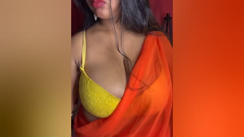 Media: A video of a woman with medium skin tone, wearing a yellow lace bra and a red-orange sari, with long dark hair and red lipstick, against a warm-toned background.