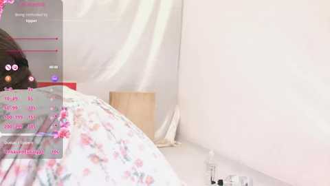 Video of a minimalist bedroom with white walls, a floral bedspread, and a wooden nightstand. The room is bathed in soft light, creating a serene atmosphere.