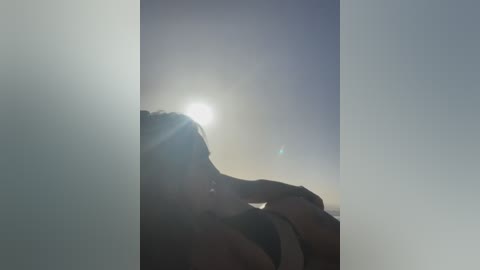 A video captures a silhouette of a person leaning against a window, bathed in bright sunlight, with a blurred, soft-focus background.