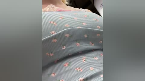 Media: A close-up video shows a woman in a light blue, ribbed, floral-patterned top, revealing a slight cleavage. Her pale skin and blonde hair are partially visible.