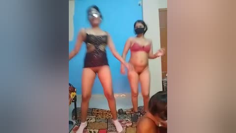A video shows two women in lingerie, one with a black mask, standing in a room with blue walls.