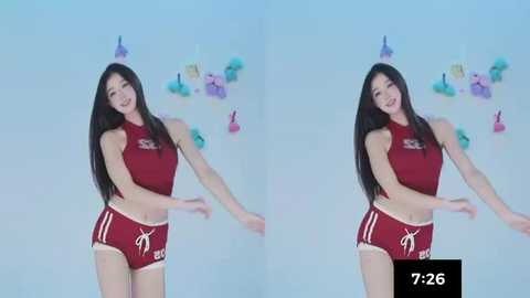 Video of an East Asian woman with long black hair, fair skin, wearing a red sleeveless crop top and matching shorts, dancing against a light blue backdrop with colorful balloon decorations.